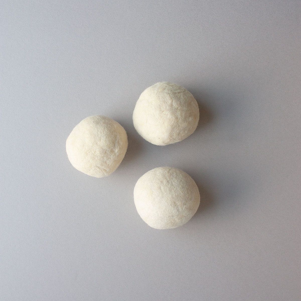 Three white felted wool dryer balls are arranged in a triangle on top of a gray background.