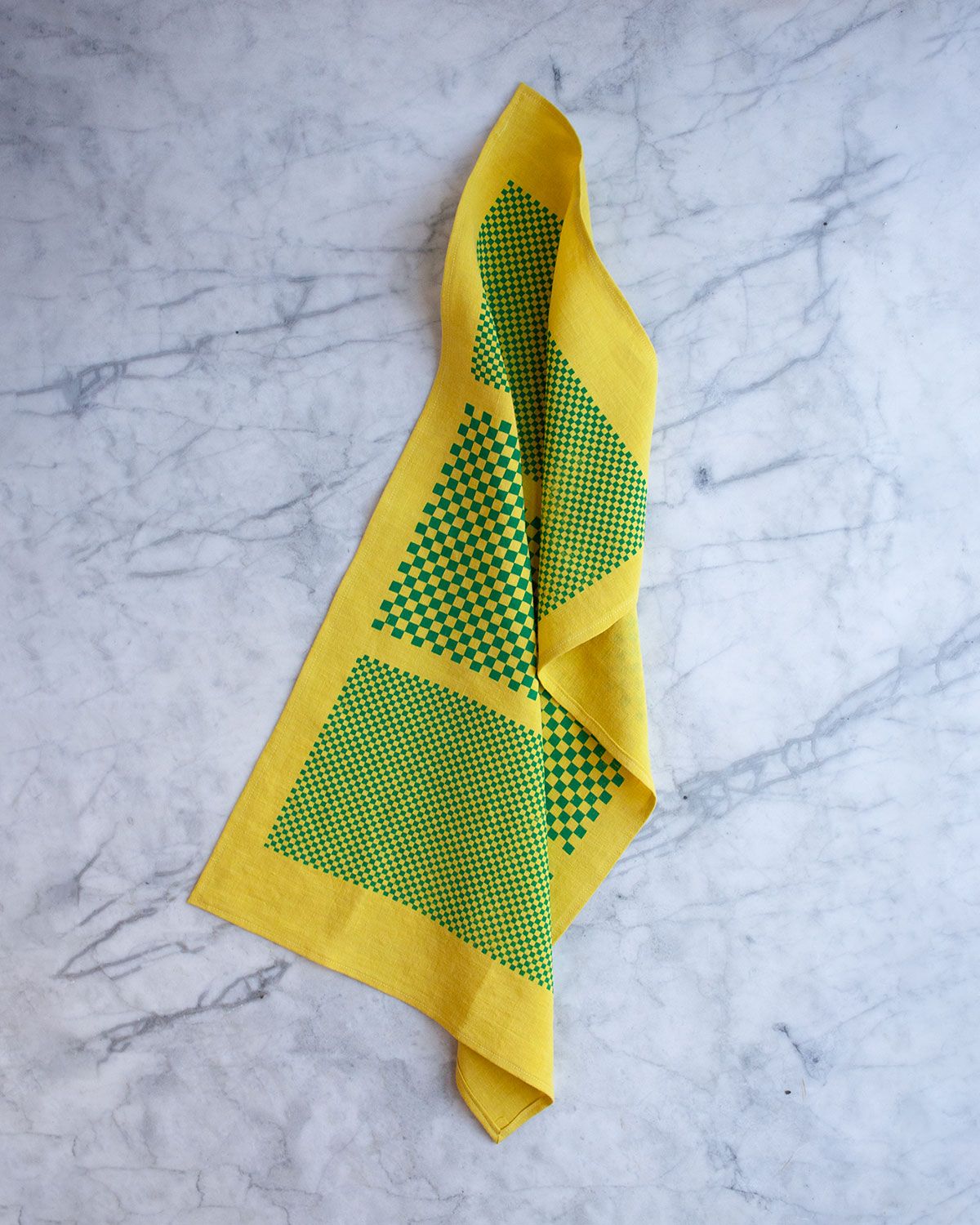 "Acid green" tea towel is shown gently tousled atop a marble surface.