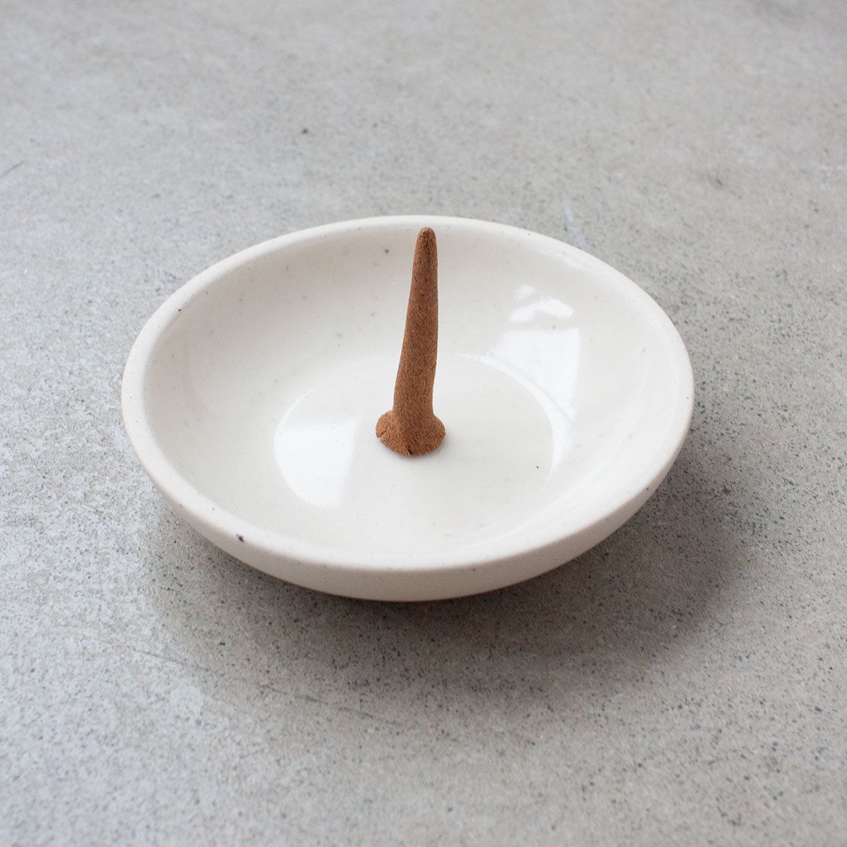 Single incense cone standing in a white dish on a concrete surface.