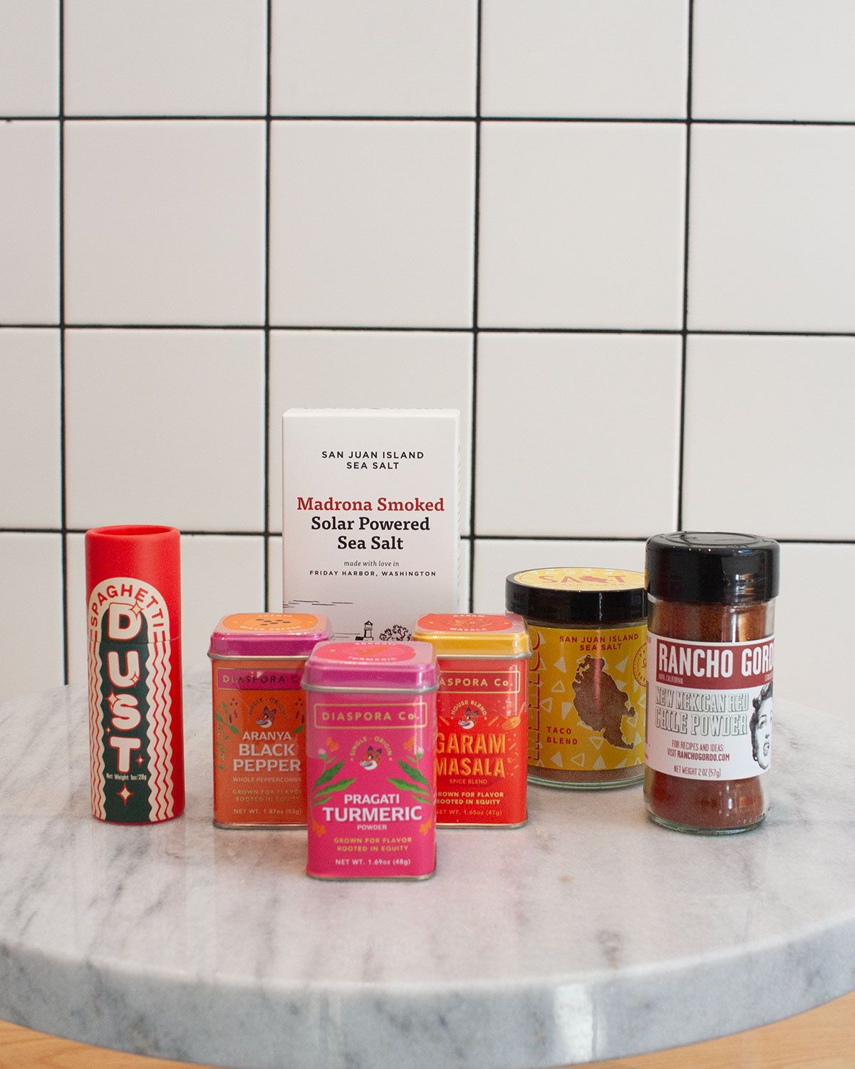 Various spices and salts arranged on a marble table top against a white tile background.