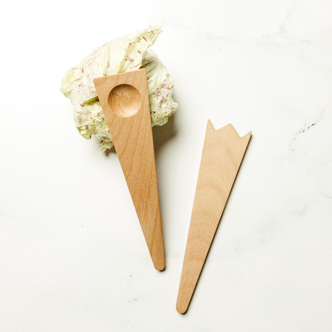 Two wooden salad servers placed on a head of radicchio on a beige background.